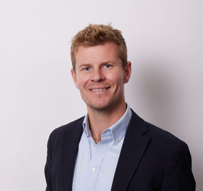 Profile picture of a man smiling wearing a black coat and light blue shirt