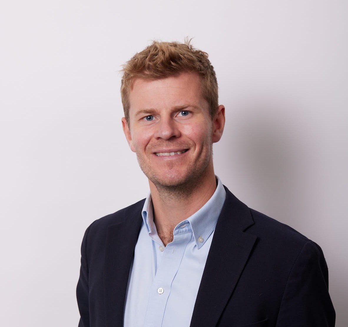 Profile picture of a man smiling wearing a black coat and light blue shirt