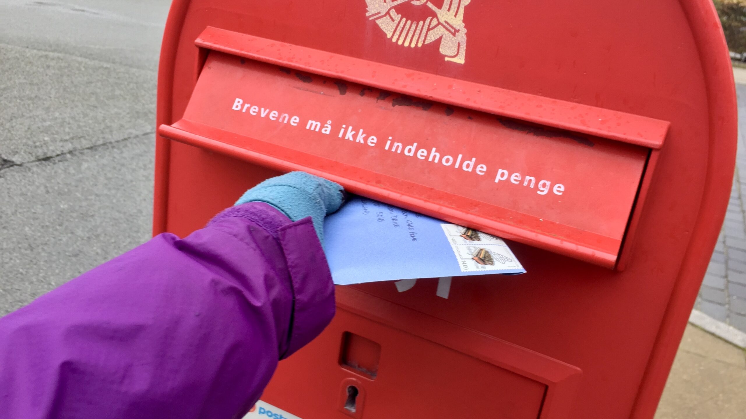 A hand putting a letter inside a red mail box