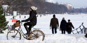 Winter in Copenhagen Women cycling in winter snow clothes while people walk on snow