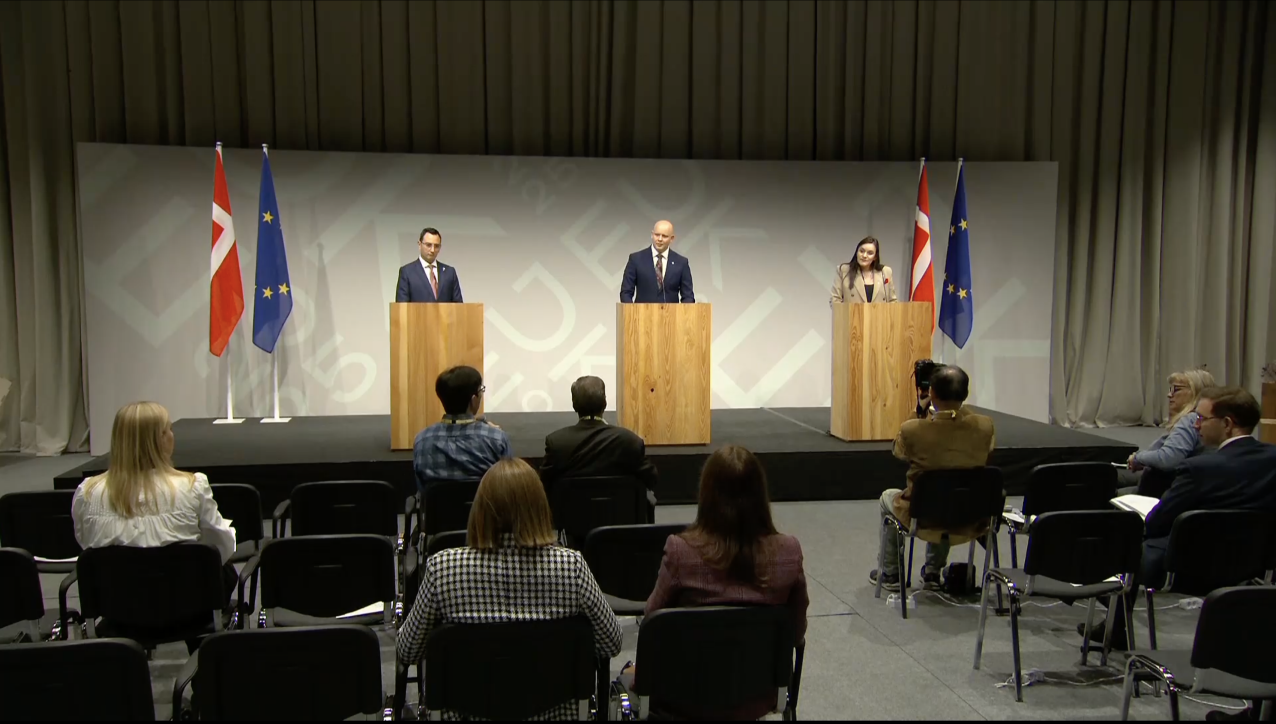 3 people standing at a podium with audience sitting