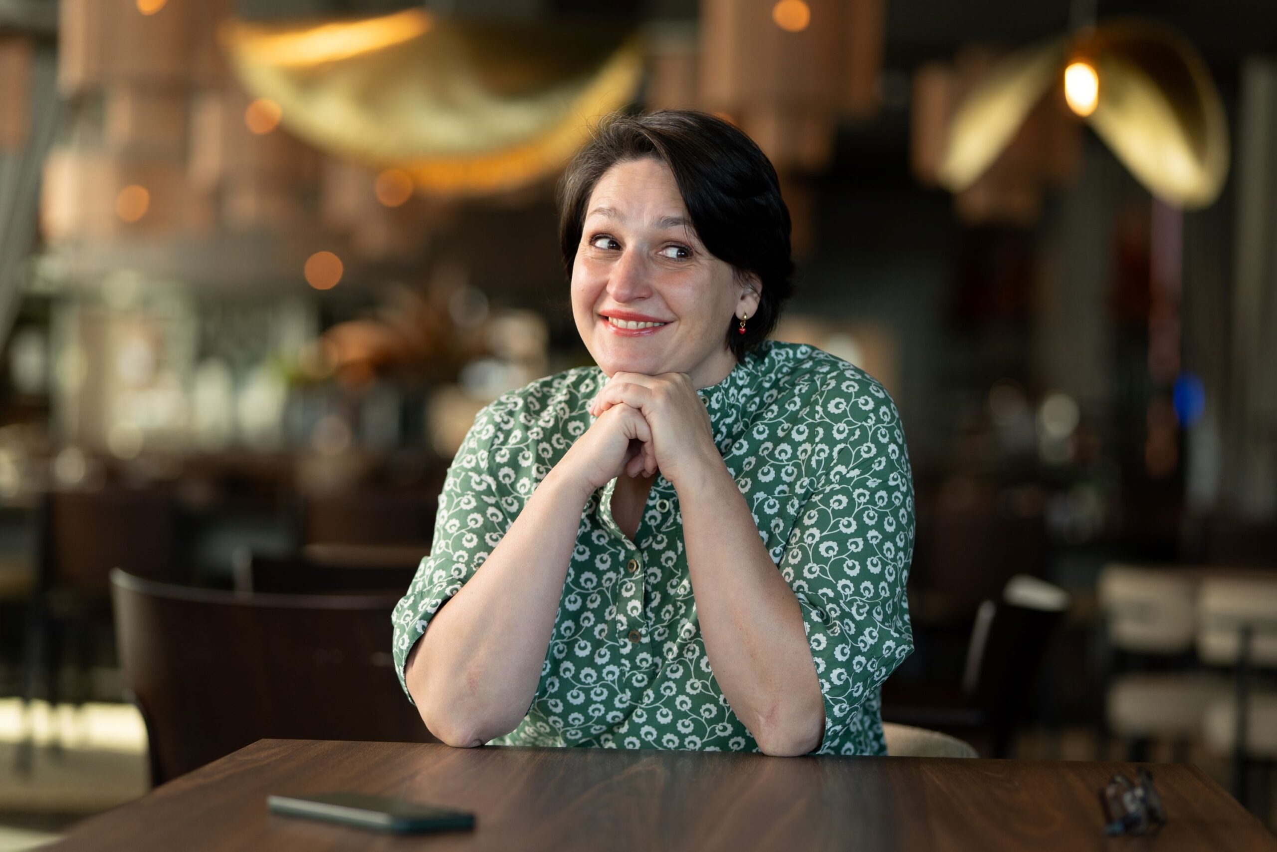 Woman sitting at the table wearing a green dress and smiling at the camera