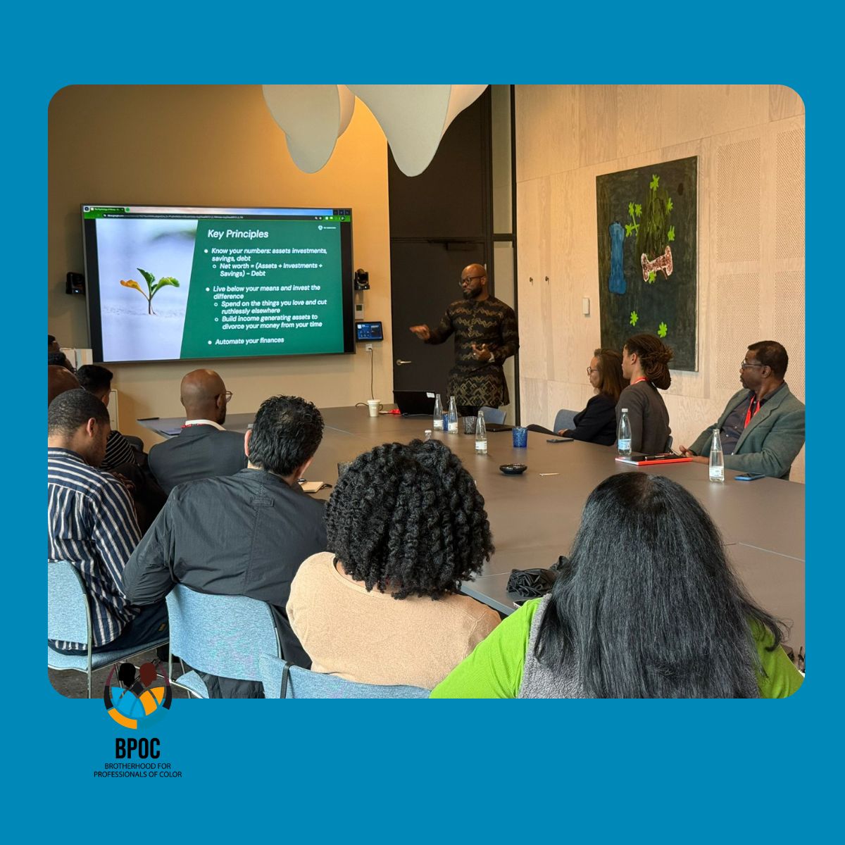 A presentation with a screen being presented by a man to a group of people sitting at a large table