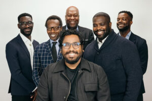 Brotherhood 6 men in black suits on white background smiling at the camera