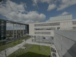 Modern campus buildings from above Aerial view of a modern university campus with concrete and glass buildings surrounding a green courtyard, under a partly cloudy sky.