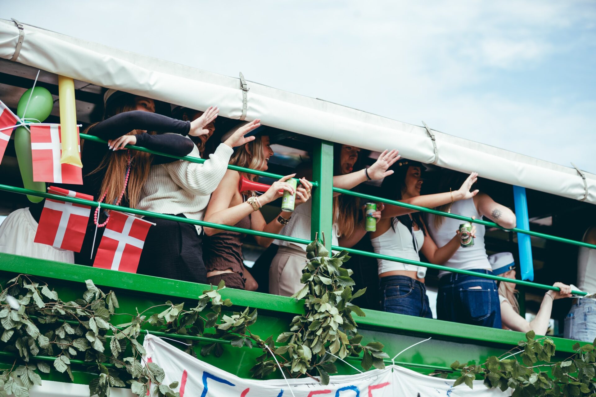 Celebrating on a graduation truck Young women in white student caps celebrate on a green-railed graduation truck decorated with Danish flags and balloons, cheering and holding drinks as they ride through town