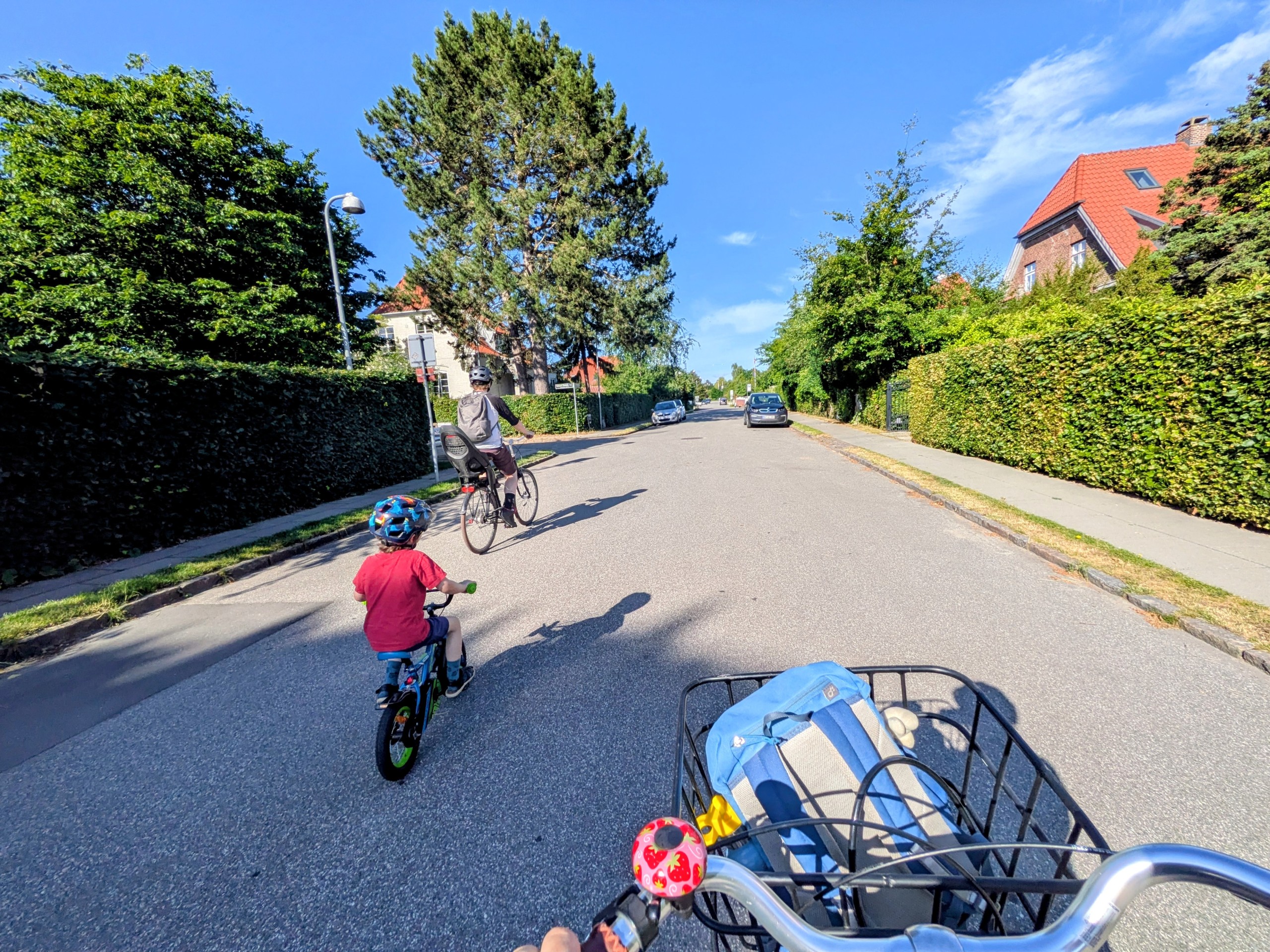 Handlebar view of a family cycling down a quiet residential street lined with tall hedges