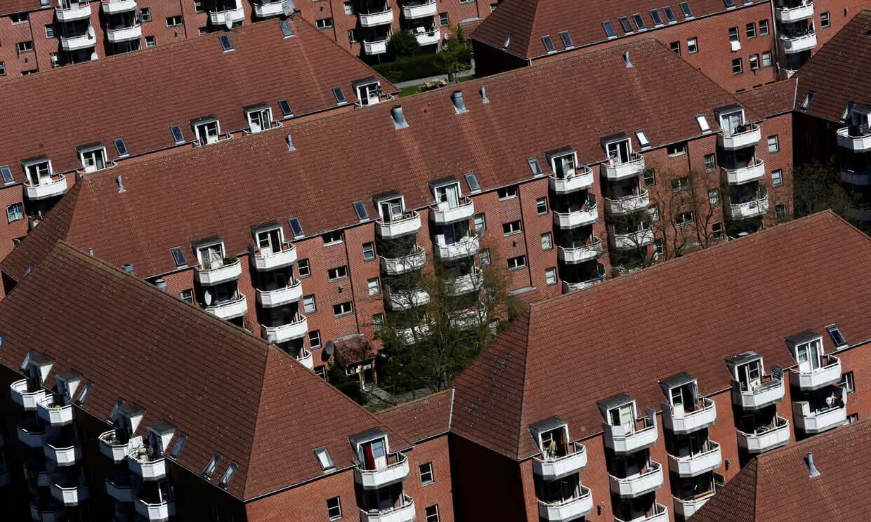 Aerial view of densely packed red-brick apartment buildings with white balconies and red-tiled roofs, with small courtyard trees visible between the blocks.