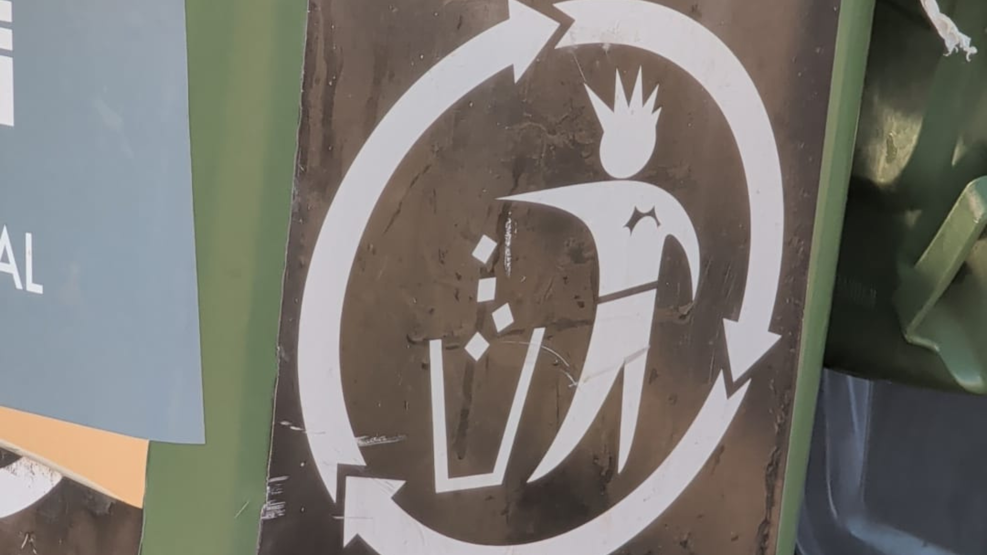 Close-up of a Roskilde Festival recycling symbol showing a stylised crowned figure inside circular arrows, printed on a brown bin