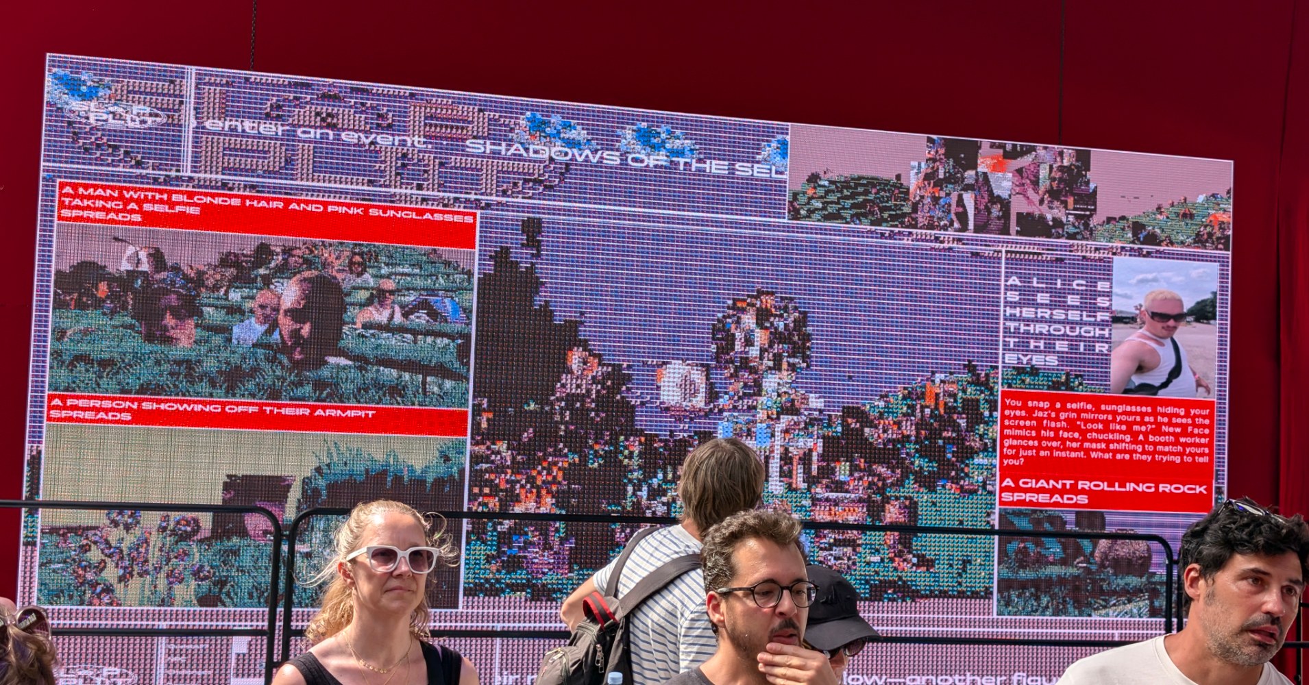 Festival visitors walk past a large red digital screen displaying an AI art installation titled 'Shadows of the Self', showing fragmented crowd imagery with AI-generated captions.