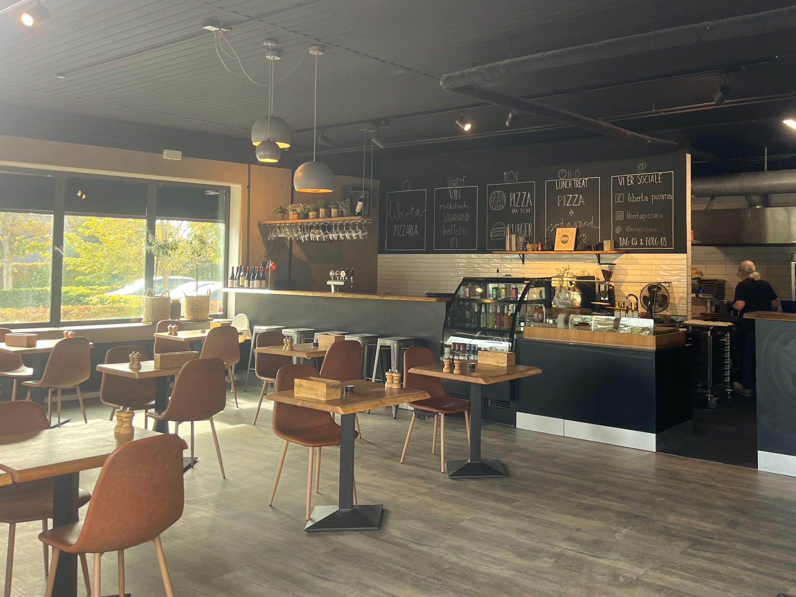 Interior of Liberta Pizzaria with wooden tables, brown chairs and chalkboard menus above the counter
