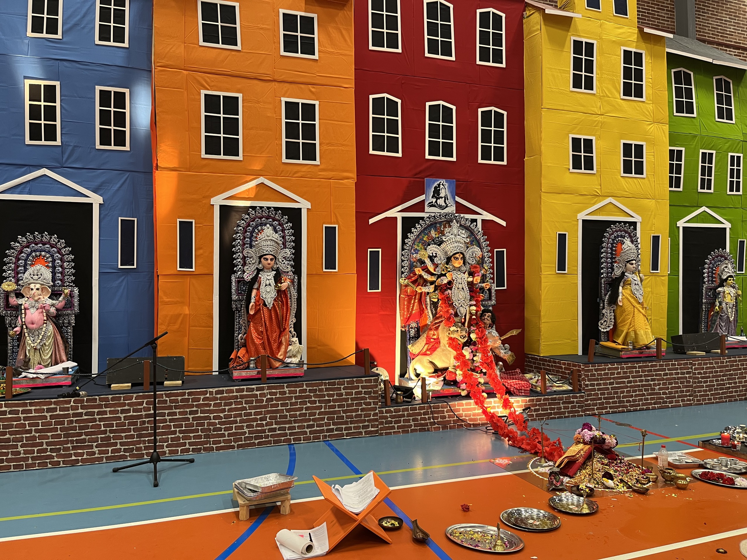 A Durga Puja pandal styled like the colourful blue, orange, red, yellow and green townhouses of Nyhavn, with an idol of a deity in each doorway and puja offerings laid out on the floor in front.